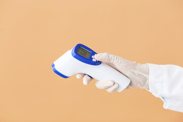Hand of doctor with infrared thermometer on color background