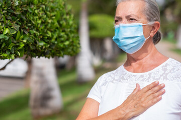 Coronavirus. Mature woman wearing surgical mask to avoid contagion of Covid-19 greets with hand on his heart