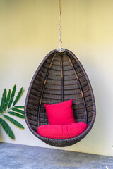 Wicker swing with a red pillow hanging near stone wall on the tropical island Koh Phangan, Thailand
