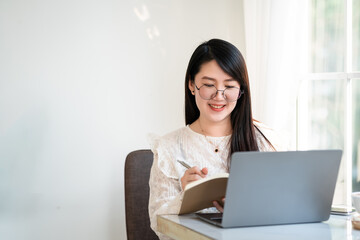 Happy of asian freelance people Businesswoman Taking written Notes to on notebook casual working with laptop computer with a coffee cup mug and smartphone at the cafe,Business Lifestyle