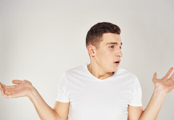 Fototapeta premium A man in bewilderment gestures with his hands on a light background in a white T-shirt cropped view