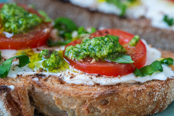 Delicious toasted bread with white cream cheese, green wild garlic and tomato on plate, close up