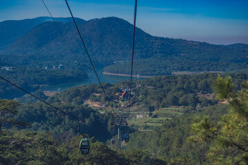 Circulating cable car between Dalat bus station and Robin Hill Truc Lam Vietnam. Intermediate support tower. Picturesque landscape view. Mountain lake. Pine forest tree tops, clear sky. Collection