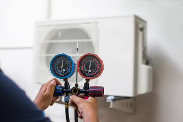 Air repair mechanic using measuring equipment for filling industrial factory air conditioners and...