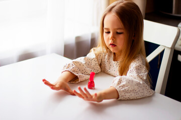 Little girl paints her nails with pink nail polish. Cute toddler girl playing with colorful nail polish doing manicure. Cosmetics and beauty concept.