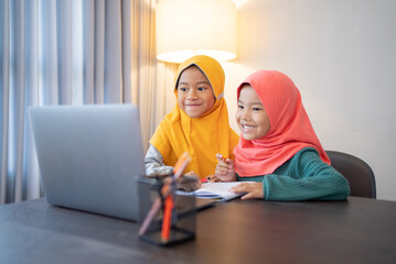 happy two muslim children wearing head scarf smiling while using laptop computer at home