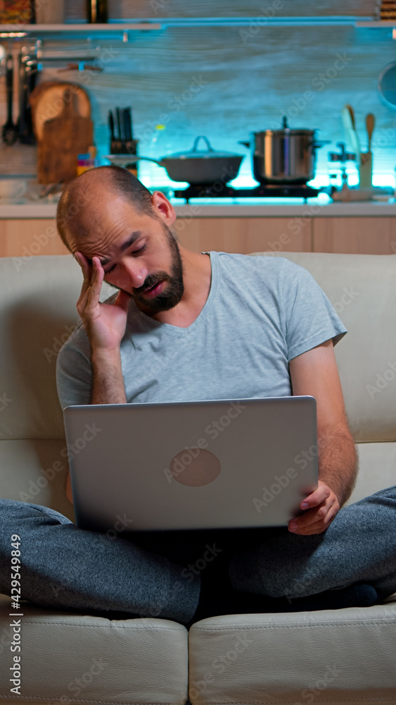 Poster tired man in pajams browsing on internet lifestyle information using laptop computer sitting on sofa