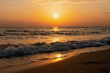 Fototapeta na wymiar Colorful sunset on a sandy beach, waves with foam on the sand. Ocean, coast. Soft selective focus, defocus