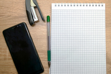 an open notepad for writing a fountain pen a stapler and a smartphone on the table