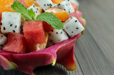 Tropical fruit salad with dragon fruit, watermelon and orange served in half a dragon fruit.