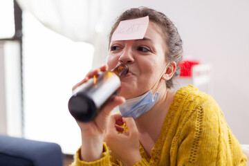 Happy woman gesturing playing name game with multiethnic friends having sticky notes on forehead wearing face mask keeping social distancing. Diverse group of people having fun at new normal party