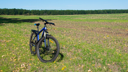 Fototapeta na wymiar Mountain bike. bike stands on in the field. A mountain bike stands on a field path with green grass. cycling. outdoor cycling activities. space for text. editorial, Ukraine, Kiev region 2020