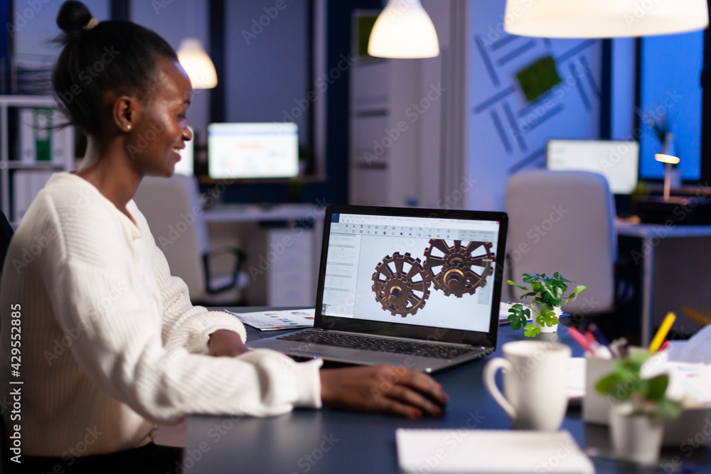 Aufkleber african engineer working late at night on a 3d model of industrial gears at laptop doing overtime in