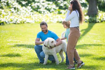 Happy family playing with dog resting together on the green grass, having fun outdoor.