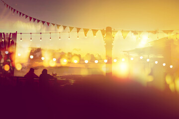 two friends watching sunset at restaurant on the beach, blurred bokeh light on sunset with yellow string lights decor in beach restaurant