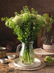 A bouquet of wild flowers in a glass jug on a wooden rustic table. Rustic style