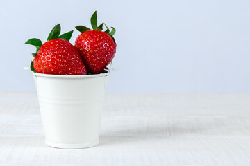 Fresh ripe strawberries in a small white bucket on a white wooden table. 