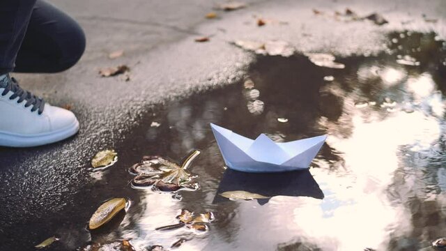Child puts a paper boat into the water. Kid playing with paper boat ship. Paper fleet. Happy family fantasy, childhood dream, adventure and travel concept.