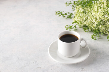 A cup of coffee and a bouquet of wild flowers on a white table with blank space on the left