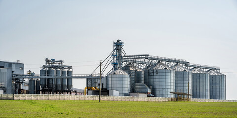 Obraz premium Modern Granary elevator. Silver silos on agro-processing and manufacturing plant for processing drying cleaning and storage of agricultural products, flour, cereals and grain. seed cleaning line