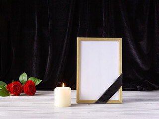 The concept of remembrance, funerals, and condolences. Photo frame with black mourning ribbon, candles and flowers.