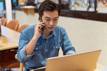 Asian man working, listening on the phone in a coffee shop