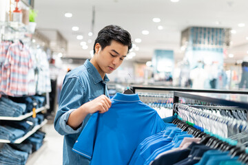 The smart Asian man is choosing clothes in the clothing store in the mall,