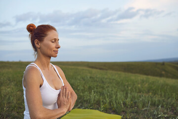 Fototapeta na wymiar Relaxed mature woman practicing meditation on quiet green meadow trying to reach inner harmony