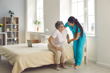 Fototapeta premium Caring for the elderly. Female caregiver who cares for an elderly woman in a nursing home helps her get out of bed. Concept of support and daily life in a nursing home
