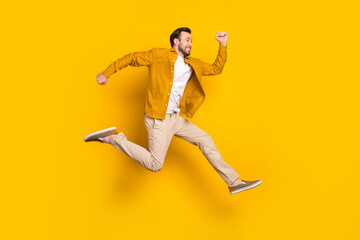 Full length photo of funky cute young guy wear casual clothes jumping running looking empty space smiling isolated yellow color background