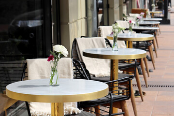 Street cafe with empty tables outdoor, city during coronavirus pandemic. Vases of flowers on a tables and vintage wooden chairs with warm plaids