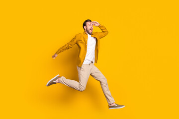 Fototapeta na wymiar Full length photo of cute charming guy wear casual clothes jumping arm forehead looking empty space isolated yellow color background