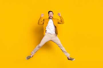 Fototapeta na wymiar Full length photo of handsome lucky young guy wear casual clothes jumping rising fists smiling isolated yellow color background