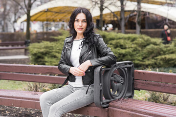 Beautiful brunette woman with curly hair posing outdoors while sitting on a bench