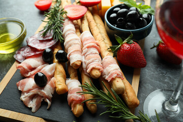 Board with grissini and snacks, and wine on black smokey table