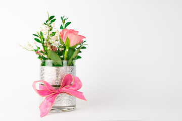 Small vase with pink bow and rose flowers, white background with copy space