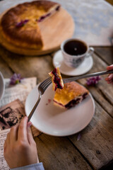 The round pie is cut into pieces. Inside, the filling is made of cherries and sugar. On a wooden table there are dishes, a cup of tea. Berries and flowers are laid out.