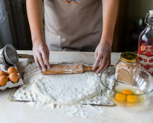 Hands of a girl on a wooden table in an apron knead the dough. Around the flour, eggs, salt.