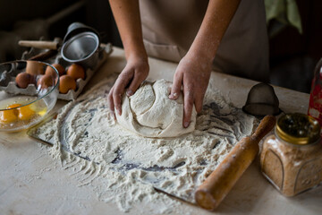 Obraz na płótnie Canvas Hands of a girl on a wooden table in an apron knead the dough. Around the flour, eggs, salt.