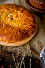 Rustic table made of rough planks. There is a plate with a round pie on it. Cherry and sugar pie filling. next to dishes and berries.