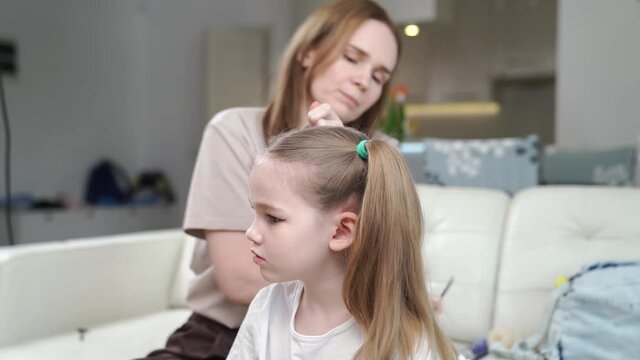 Mom combs her daughter and makes two tails, hurry, it turns out not immediately. preparing the child for the performance on stage. eye makeup.