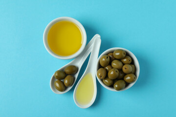 Spoons and bowls with olives and oil on blue background