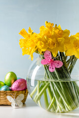 Yellow daffodils in round glass vase on table with light blue background. Easter theme.