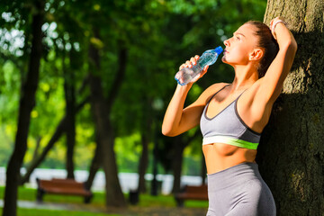 Running Concepts. Portrait of Sexy Caucasian Female Drinking Still Water During Exercises Near Tree Outdoors At Daytime.