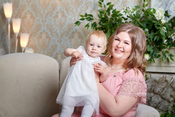 Portrait of a little blonde girl and plumb chubby mother in beautiful dress. Family in studio during photo shoot