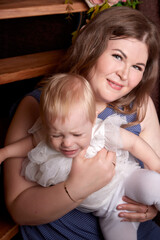 Portrait of a little blonde girl and plumb chubby mother in beautiful dress. Family in studio during photo shoot