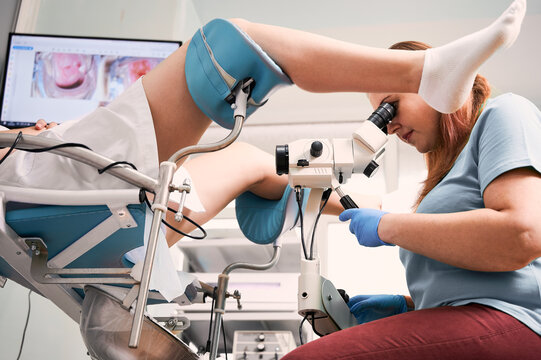 Side view of doctor using colposcope while examining woman in gynecological clinic. Patient laying in chair while doctor doing colposcopy examination. Concept of gynecology, medical examination.