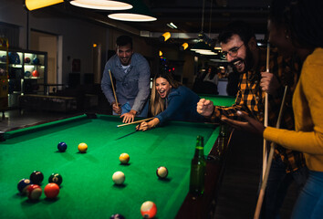 Four smiling friends in bar playing billiard together.