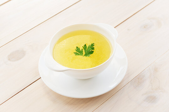 Homemade Chicken Broth In A White Plate On A Wooden Table.