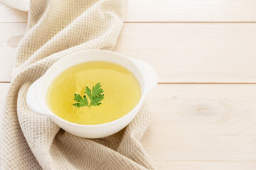 Homemade chicken broth in a white plate on a wooden table. Horizontal orientation, copy space.